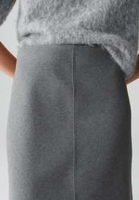 Grauer Woll-Bleistiftrock mit glatter Textur und mittigem Nahtdetail, ergänzt durch einen flauschigen hellgrauen Pullover darüber.