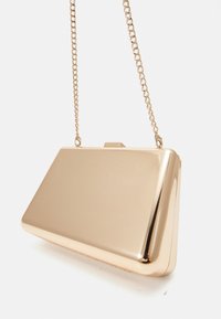 Złota metaliczna kopertówka o smukłym, prostokątnym kształcie i gładkim wykończeniu. Posiada złoty łańcuszkowy pasek i zapięcie na zatrzask z góry.