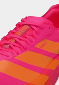 Knallpinker Sportschuh mit orangen Streifen und Schnürsenkeln, mit einem durchsichtigen Zungenetikett mit oranger Schrift "ADIZERO".