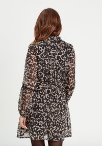 Robe noire et beige à motifs, avec un col, des manches longues et une taille élastique, dotée d'une jupe évasée.