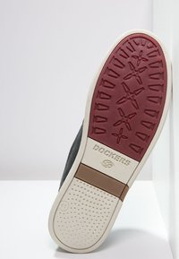 Semelle de sneaker noire avec une section en caoutchouc rouge texturé et un contour blanc. Présente le logo "DOCKERS" et un indicateur de taille (41). Motif de grip texturé.