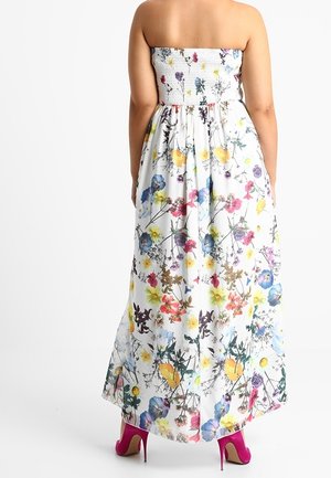 Vrouw draagt een strapless witte maxi-jurk met meerkleurige bloemenprint en felroze hoge hakken, van achteren gezien.
