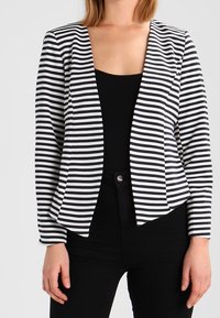 Czarny i biały w paski żakiet o dopasowanym kroju, z otwartym przodem i długimi rękawami. Nosi się go na jednolitym czarnym topie, w zestawieniu z czarnymi dołem.