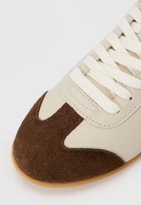Baskets en cuir et en daim avec une tige beige, un bout en daim marron et des lacets crème. Semelle en caoutchouc avec une finition texturée.