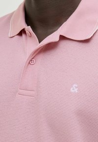 Ružičasta polo majica s teksturiranom tkaninom, s ovratnikom, jednim gumbom na zatvaranju i suptilnim izvezenim logotipom na prsima.