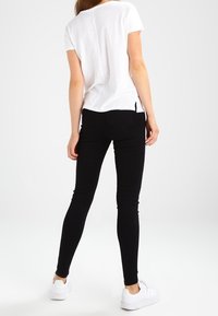 Camiseta blanca de manga corta con un corte holgado, combinada con jeans negros ajustados y zapatillas blancas. Diseño sencillo con aberturas laterales en el dobladillo.