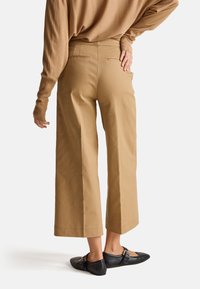 Beżowe spodnie o szerokich nogawkach z wysokim stanem, z tylnymi kieszeniami, szwami i gładką fakturą. Noszone z czarnymi balerinami.