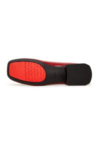 Zapato rojo con parte superior suave, suela de goma negra, puntera redondeada plana y texto en relieve en la suela para un detalle adicional.