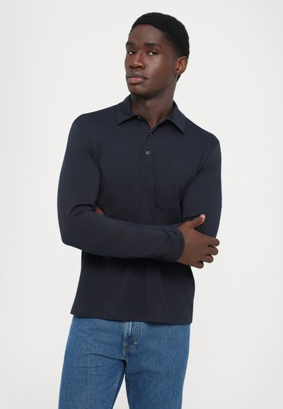 Navy long-sleeve polo shirt with a collar, two-button placket, and a chest pocket, paired with light blue jeans. Smooth fabric texture.