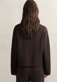 Brązowy krótki sweter z luźnym krojem, wykonany z miękkiego materiału, z okrągłym dekoltem i opadającymi ramionami, w komplecie z dopasowanymi spodniami.
