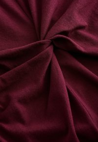 Burgundská pletená látka, zkroucená do spirály, má jemnou strukturu a hladký povrch s mírným elastickým efektem, přičemž vykazuje konzistentní barvu a vazbu.