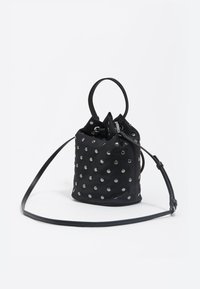Bolso tipo cubo de cuero negro con detalles de tachuelas plateadas, cierre con cordón y correa desmontable para llevar cruzado. Forma redonda, textura suave.