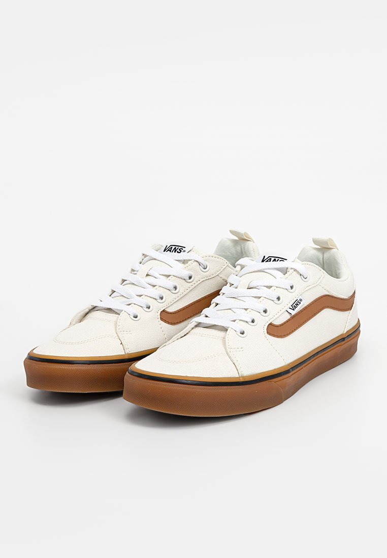 Zapatillas de lona blancas con detalles en marrón, diseño con cordones, suela de goma y cuello acolchado. Presenta el logo de Vans en la lengüeta.