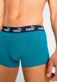 Teal boxer shorts made of soft fabric with a navy waistband featuring white Puma logo. Close-up view highlighting fit and texture.