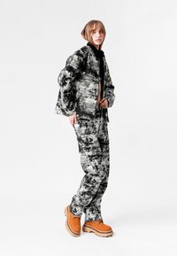 Conjunto de tela de estampado en blanco y negro que incluye una chaqueta con cremallera y pantalones a juego, complementado con calzado naranja y acentos de herrajes redondos.