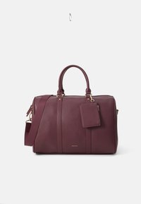 Maroon leather duffle bag with two handles, detachable shoulder strap, gold-tone hardware, and a removable tag. Textured surface and structured shape.