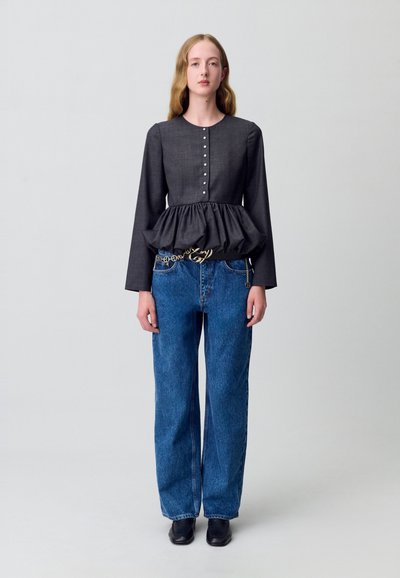 Blusa peplum grigia scura con maniche lunghe, chiusura a bottoni e finitura testurizzata, abbinata a jeans in denim blu a vita alta. Scarpe nere.