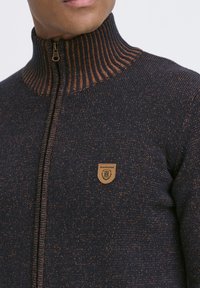 Mornarčki pleteni pulover s narančastim rebrastim ovratnikom, z zadrgo po celotni dolžini spredaj in usnjenim odtisom z logotipom leva na levem prsnem delu.