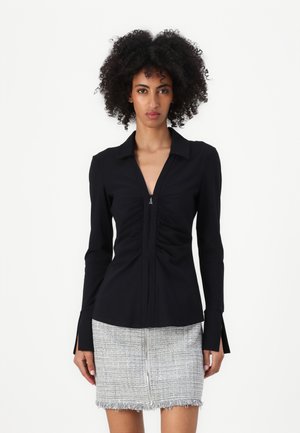 Maglietta nera a maniche lunghe con un design arricciato verticale, colletto a punta e dettaglio con zip sullo scollo. Tessuto liscio e vestibilità sartoriale.