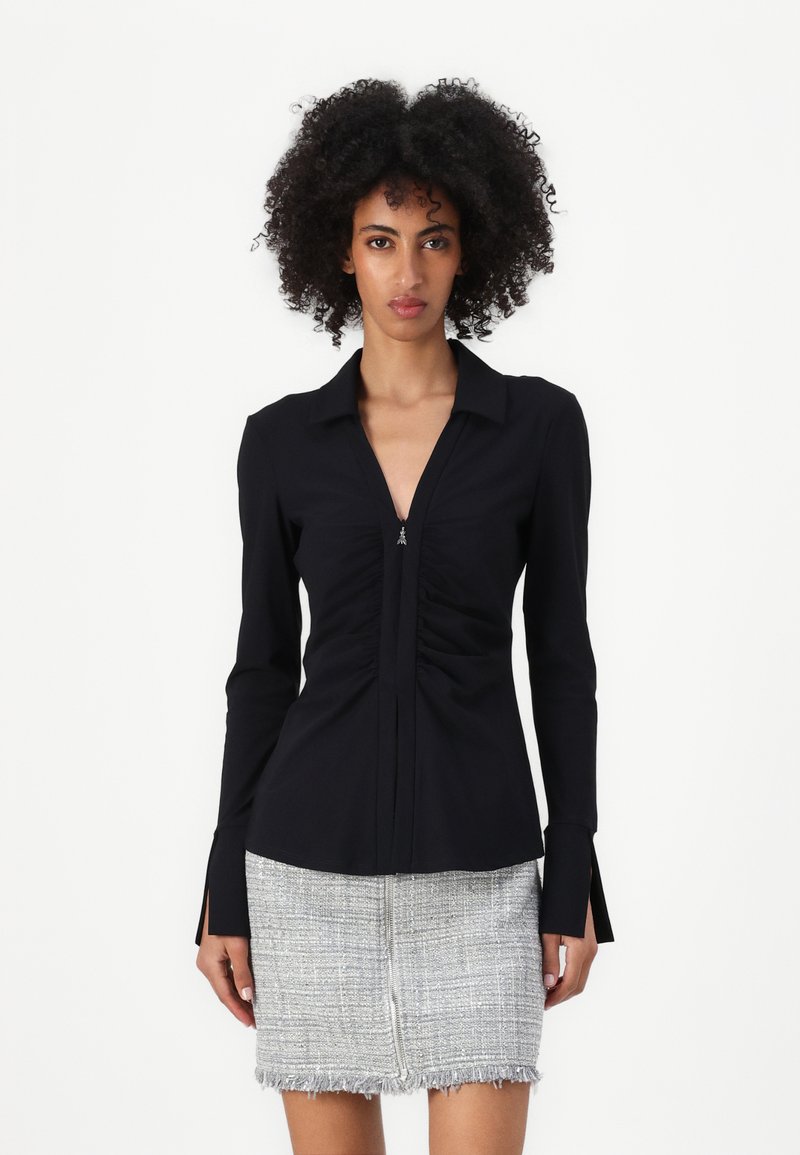 Maglietta nera a maniche lunghe con un design arricciato verticale, colletto a punta e dettaglio con zip sullo scollo. Tessuto liscio e vestibilità sartoriale.