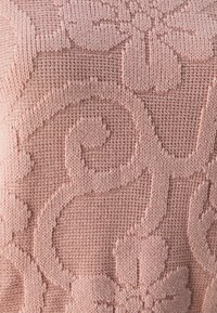 Le tissu tricoté de couleur rose pâle présente un motif floral imprimé en relief ainsi que des volutes. La texture est lisse avec un tissage fin et une profondeur subtile.