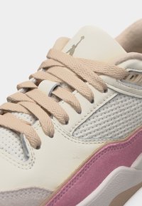 Κοντινό πλάνο λευκού αθλητικού παπουτσιού με μπεζ κορδόνια, λευκές πλευρές από δίχτυ, ροζ πάνελ από σουέντ και μικρό λογότυπο στη γλώσσα του παπουτσιού.