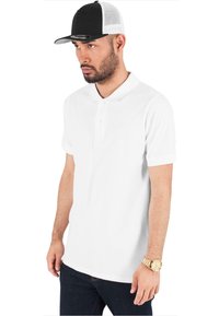 Witte poloshirt met een klassieke kraag en korte mouwen, gecombineerd met een zwarte pet met een gaas achterdeel en een flat visor.