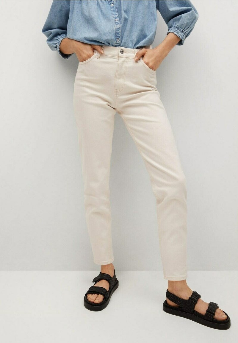 Vaaleanbeiget, kapeat farkut, joissa on sileä pinta, korkeavyötäröinen leikkaus ja viisitaskuinen malli, yhdistetty mustiin, monistrappisiin sandaaleihin.