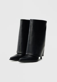 Μαύρες δερμάτινες μποτάκια αστραγάλου με κομψό σχεδιασμό, μυτερή μύτη και ψηλό, λεπτό τακούνι. Ο άξονας είναι λείος και επεκτείνεται πάνω από τον αστράγαλο.