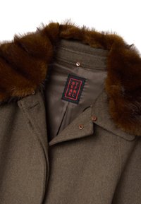 Cappotto in lana verde oliva con colletto in pelliccia sintetica marrone, fodera color sabbia e bottoni marroni. L'etichetta riporta "STEFANEL" in rosso su sfondo nero.