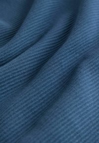 Nærbillede af blødt, ribbet blåt stof med blide folder, der skaber skygger og detalje i teksturen.