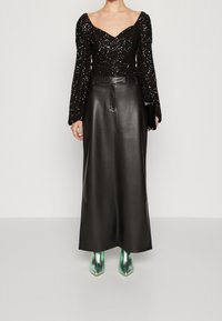 Svart paljetterad långärmad topp med hjärtformat dekolletage, kombinerad med en svart lädermaxikjol och metalliska gröna ankelstövlar.