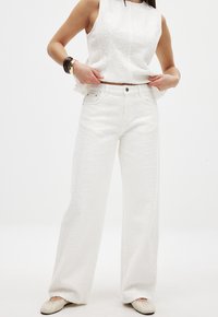 Top sin mangas texturizado blanco y pantalones de pierna ancha a juego, con un patrón sutil. El conjunto tiene un diseño casual y se complementa con zapatos ligeros.