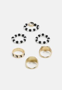 Cinco anéis: duas bandas de ouro, um em ouro com padrão yin-yang, e três anéis de contas (preto e branco), apresentando designs e texturas variadas.