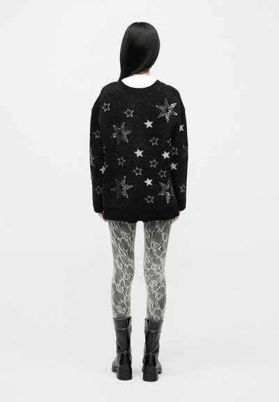 Pulover negru cu aplicații de stele argintii, asortat cu colanți texturizați cu imprimeu de șarpe. Botine negre completează ținuta.
