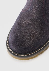 Bottine cheville en daim bleu foncé avec une finition pailletée brillante, des coutures rouges contrastantes, et une semelle en caoutchouc durable avec un détail de couture visible.