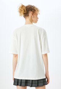Hvid bomulds T-shirt med korte ærmer, en afslappet pasform og en rund halsudskæring, båret med en gråternet, plisseret nederdel.
