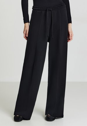 Pantaloni neri a gamba larga con vita elastica e cordino. Presentano un tessuto morbido e testurizzato e dettagli di cucitura in vista.