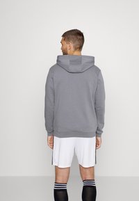 Grijze katoenen hoodie met een grote capuchon, geribbelde manchetten en zoom; gedragen met witte shorts en zwarte sokken. Minimalistisch ontwerp, geen zichtbare logo's.