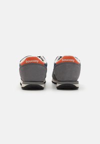 Grå semskede sneakers med sort gummisål, orange og marineblå detaljer, og en hvid polstret krave. "Saucony" vises på hælen.