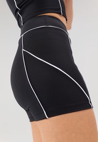 Černé sportovní šortky s kontrastním bílým prošitím, s přiléhavým střihem a hladkým, elastickým materiálem pro pohodlí a volnost pohybu.