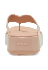 Pfirsichfarbene Gummi-Flip-Flops mit einer dicken weißen Sohle, subtilem wellenförmigen Design am Riemen und einem hervorgehobenen "CROCS"-Logo an der Seite.