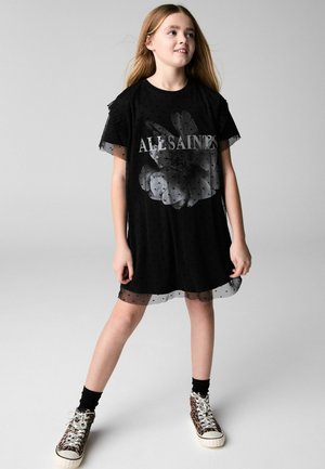 Schwarzes Kleid mit einem durchsichtigen Überzug mit Punkten, kurzen Ärmeln und einem floralen Grafikdesign; kombiniert mit Sneakers im Tiermotiv.
