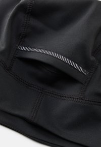 Black athletic fabric with smooth texture, featuring a discreet pocket and contrasting stitched seams. Compact and streamlined design.