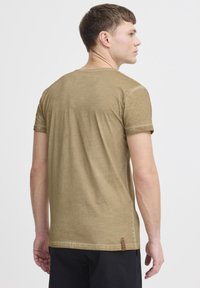 T-shirt verde oliva realizzato in tessuto morbido, con maniche corte e scollo rotondo. Leggera texture e un'etichetta di marca all'orlo.