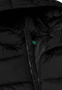 Giubbotto a vento nero con zip frontale, caratterizzato da una texture trapuntata e un'etichetta interna verde. L'interno è liscio e foderato.