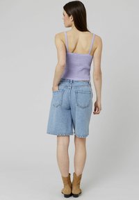 Un crop top en tricot violet avec des bretelles fines, associé à un short Bermuda en denim bleu clair, terminé par un ourlet effiloché et des bottines brunes.