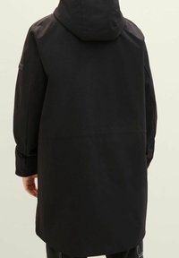 Black waterproof coat featuring a hood, loose fit, and textured fabric. Back view shows a straight hem and minimalistic design details.