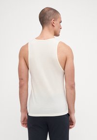 Ermeløs hvit tank topp, lett stoff, tettsittende design, rund halsutskjæring, og myk tekstur. Synlig søm og kantdetaljer.