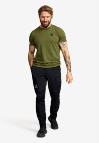Olivgrön t-shirt med kort ärm och logotyp på bröstet, tillsammans med svarta cargo-byxor med sidofickor och modern passform. Svarta skor.